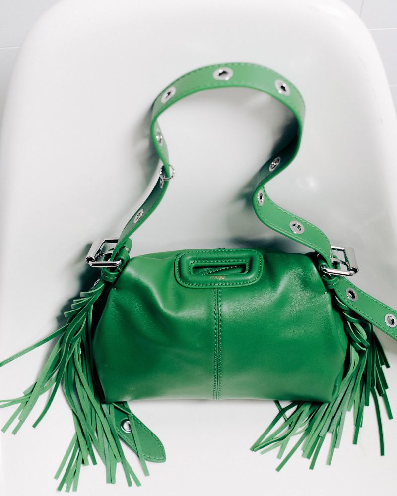 Green leather fringe purse with silver hardware, featuring a wide, studded shoulder strap against a clean, minimalist white backdrop.