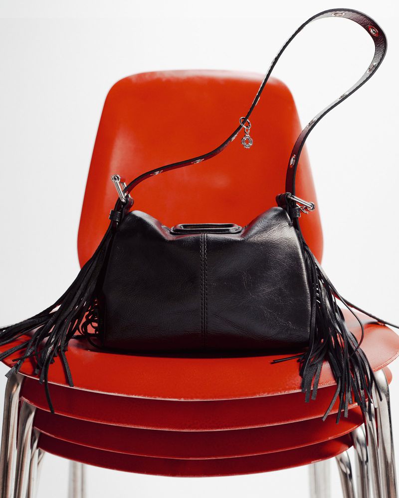 Black leather fringe purse with silver hardware on orange chairs. Fashion product shot in studio with white background.