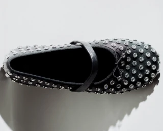 Top-down view of a black studded Mary Jane flat shoe decorated with rhinestones against a bright white background.