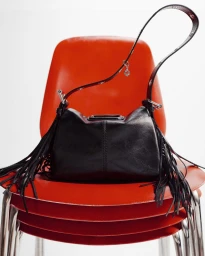 Black fringed leather handbag resting on a stack of glossy red chairs against a plain white background