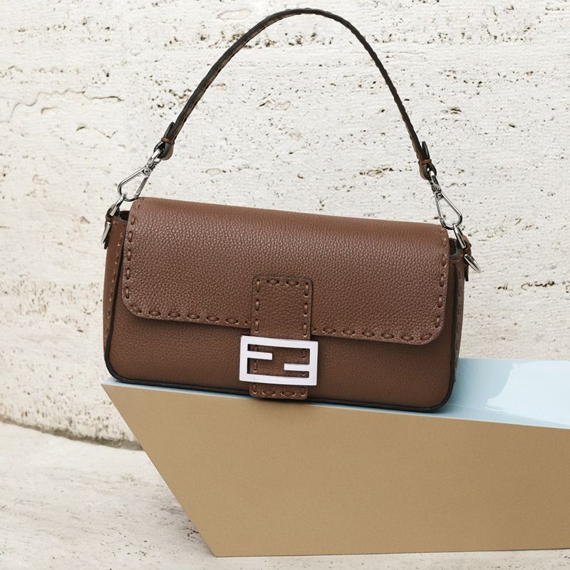 Brown leather Fendi baguette bag with a silver logo on a geometric display stand against a textured off-white wall background.
