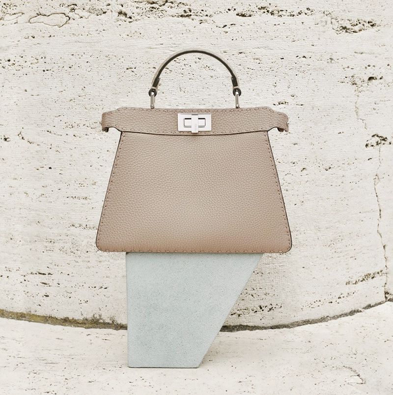Beige leather Fendi Peekaboo handbag on a light blue geometric stand against a textured white travertine wall backdrop.