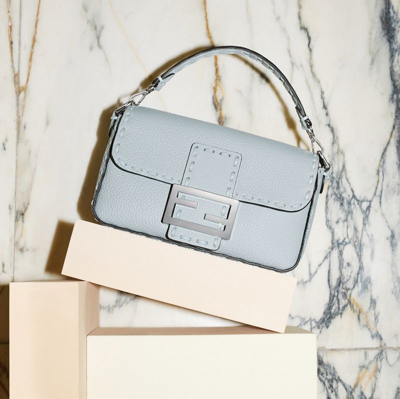 Light blue leather Fendi Baguette handbag on a pale pink cube against a marble background, studio shot for fashion editorial.