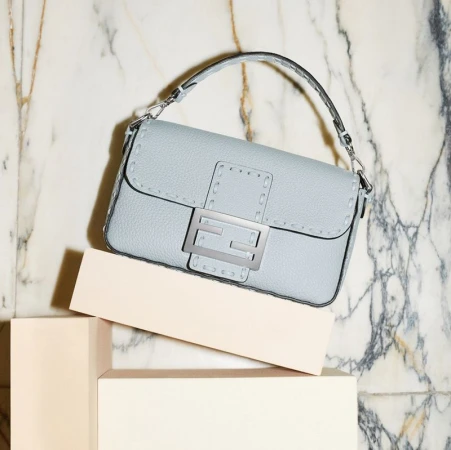 Light blue leather Fendi Baguette handbag on a pale pink cube against a marble background, studio shot for fashion editorial.