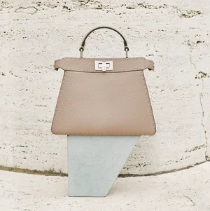 Fendi beige leather handbag resting on a grey block against a textured stone wall