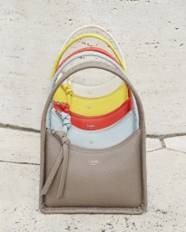 Stacked colorful leather Fendi Baguette mini handbags in taupe, blue, red, yellow and white against a textured stone wall