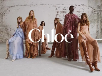 Group of female models in flowing dresses and boots posing against a rustic concrete wall for Chloé Winter 2024