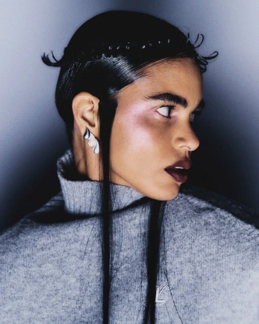 Portrait of a woman with dark hair styled back from her face and wearing a grey turtleneck sweater, glancing away from the camera.
