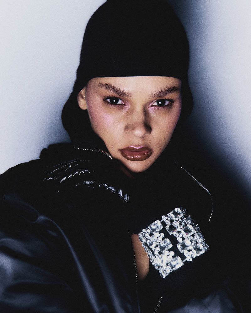 Close-up shot of a woman wearing a black beanie and jacket, adorned with a silver gemstone bracelet, against a soft, light backdrop.