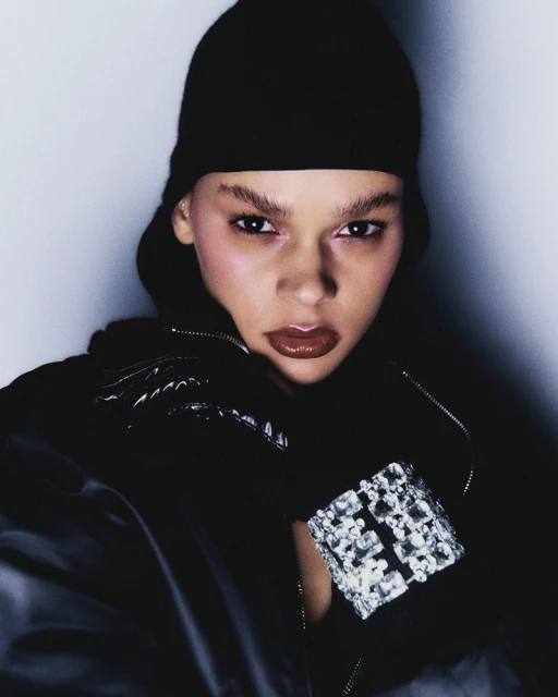 Close-up shot of a woman wearing a black beanie and jacket, adorned with a silver gemstone bracelet, against a soft, light backdrop.