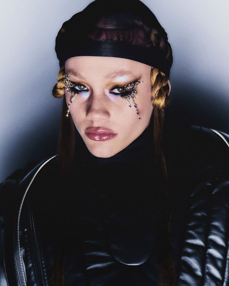 Close-up portrait of a person with makeup and a black head covering, showcasing beauty and fashion in a studio setting with dark background.