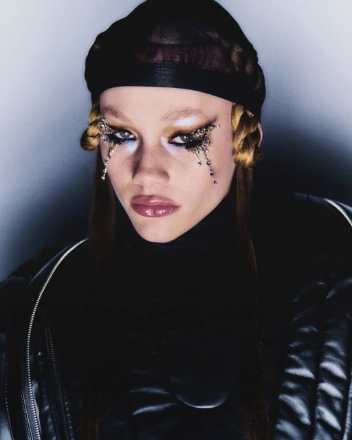 Close-up portrait of a person with makeup and a black head covering, showcasing beauty and fashion in a studio setting with dark background.
