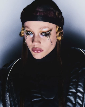 Close-up portrait of a person with makeup and a black head covering, showcasing beauty and fashion in a studio setting with dark background.