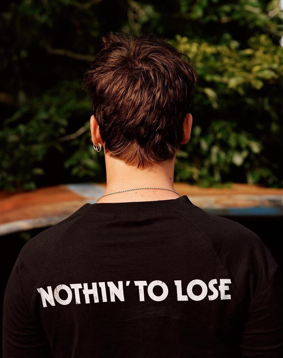 Rear view of a person with brown hair wearing a black long-sleeve shirt with white text saying NOTHIN TO LOSE.