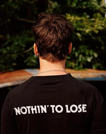 Rear view of a person with brown hair wearing a black long-sleeve shirt with white text saying NOTHIN TO LOSE.