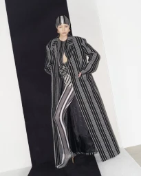 Model wearing a black and white striped long coat, matching tights, and headscarf against a studio background.