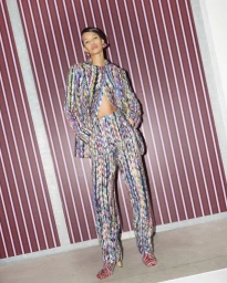 Model wearing a multicoloured patterned suit standing against a striped pink and purple wall in a fashion campaign