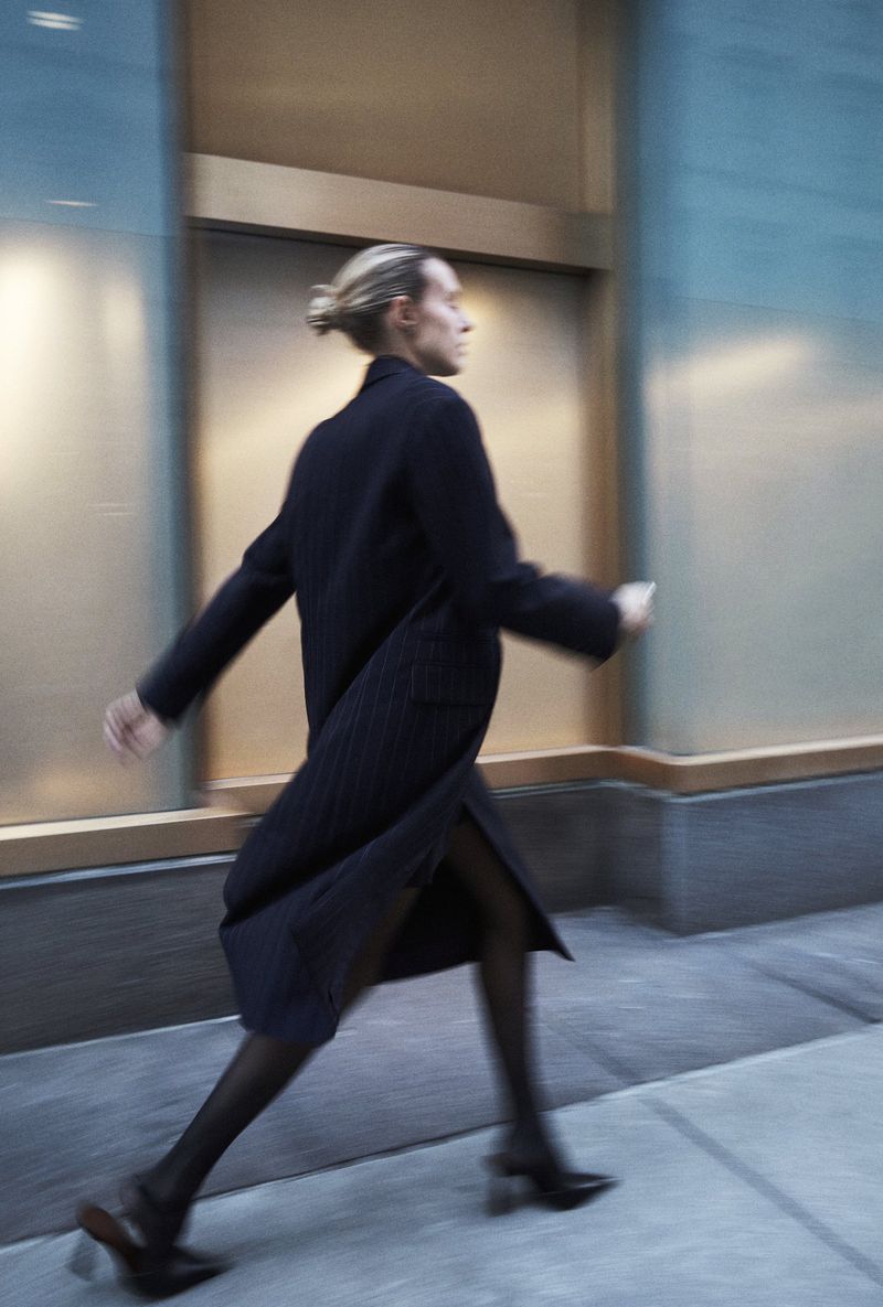 Fashionable woman in a coat strides on a city street with motion blur. The blurred background emphasizes the movement and contemporary style.
