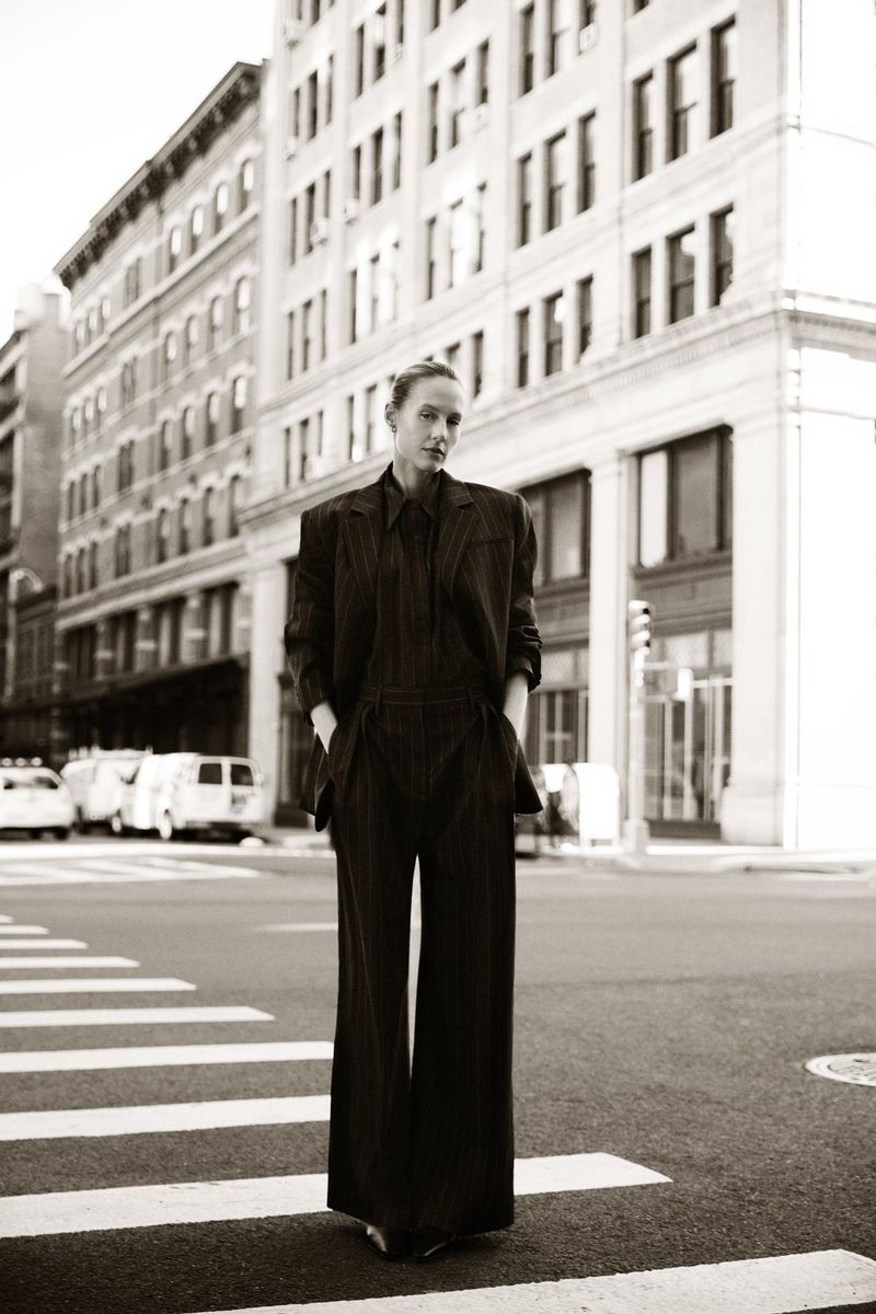 Woman in a dark suit walks in a black-and-white photo on a crosswalk in an urban setting. Tall buildings are in the background.