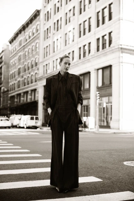 Woman in a dark suit walks in a black-and-white photo on a crosswalk in an urban setting. Tall buildings are in the background.