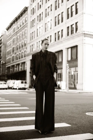 Woman in a dark suit walks in a black-and-white photo on a crosswalk in an urban setting. Tall buildings are in the background.