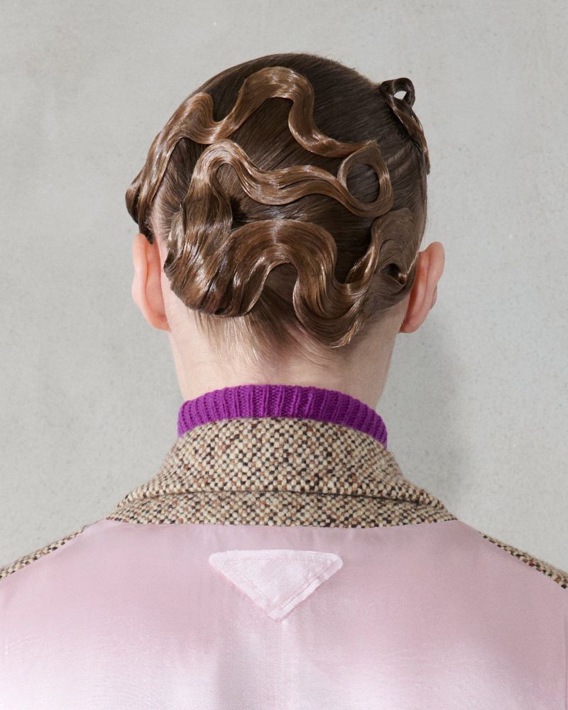 Close-up of a person with a vintage hairstyle, wearing a tweed jacket and purple top, showcasing fashion and beauty details.