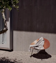 Knit shirt draped over a modern round wooden chair against a concrete wall for Trenery Autumn 2024
