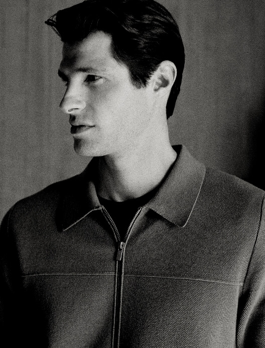 Monochrome portrait of a man wearing a zippered jacket against a neutral studio background