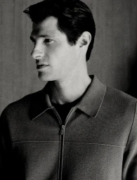 Monochrome portrait of a man wearing a zippered jacket against a neutral studio background