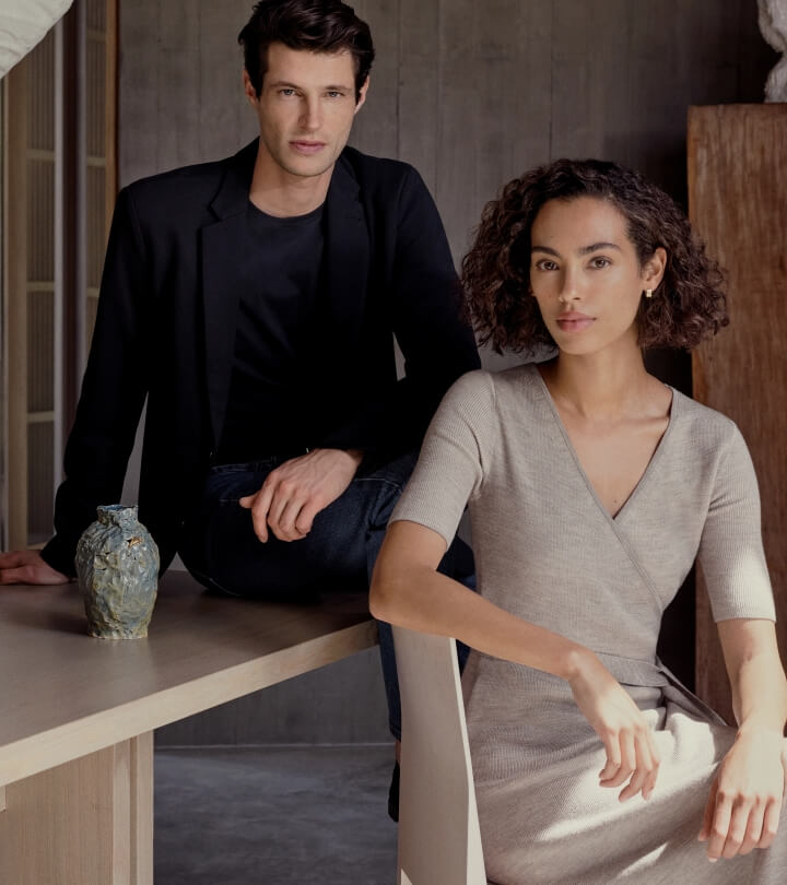 Indoor portrait of a man and a woman; the man is seated and leaning on a table next to a decorative vase, the woman is seated in a chair.