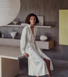 Model seated on a large wooden table in an elegant interior wearing a patterned cream midi dress
