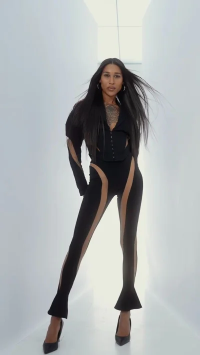 Model Gia Bab in a black fitted bodysuit with cutout panels standing in a bright white corridor for Mugler Alien Hypersense