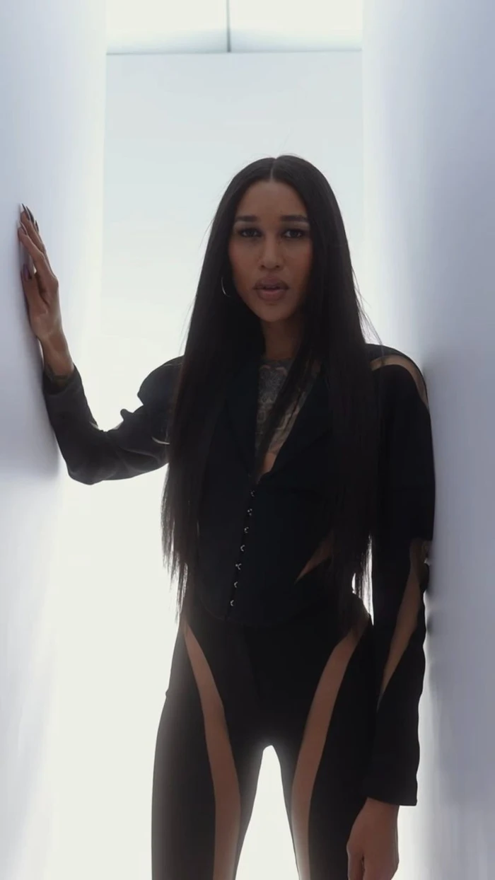 Model Gia Bab in a black fitted outfit posing in a white corridor for Mugler Alien Hypersense