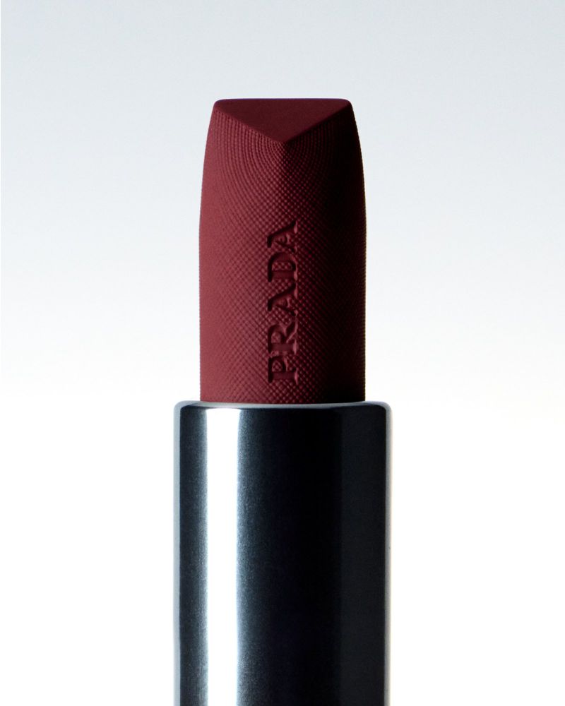 Close-up studio shot of a matte plum PRADA lipstick with black and silver casing set against a bright white background.