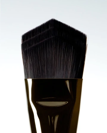 Close-up studio shot of a makeup brush with black bristles and a shiny gold handle against a clean white background.
