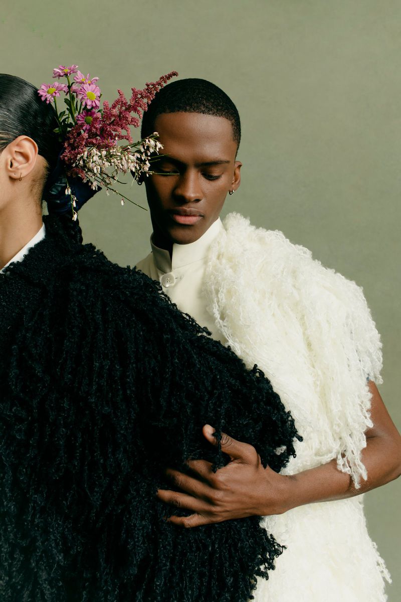 Two models wearing textured coats and fresh flowers in their hair against a solid green background