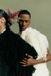 Two models wearing textured coats and fresh flowers in their hair against a solid green background