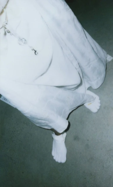 Person in white garment wearing socks and barefoot standing on a grey floor, shot from above in a high-angle, portrait orientation.