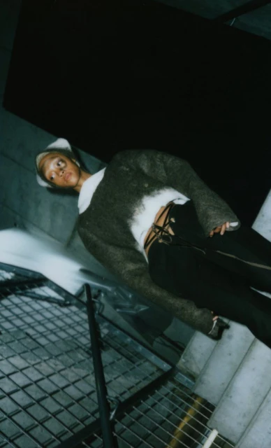 Fashionable woman poses on metal stairs wearing furry cropped sweater, black pants, and white beanie hat in an underground setting.
