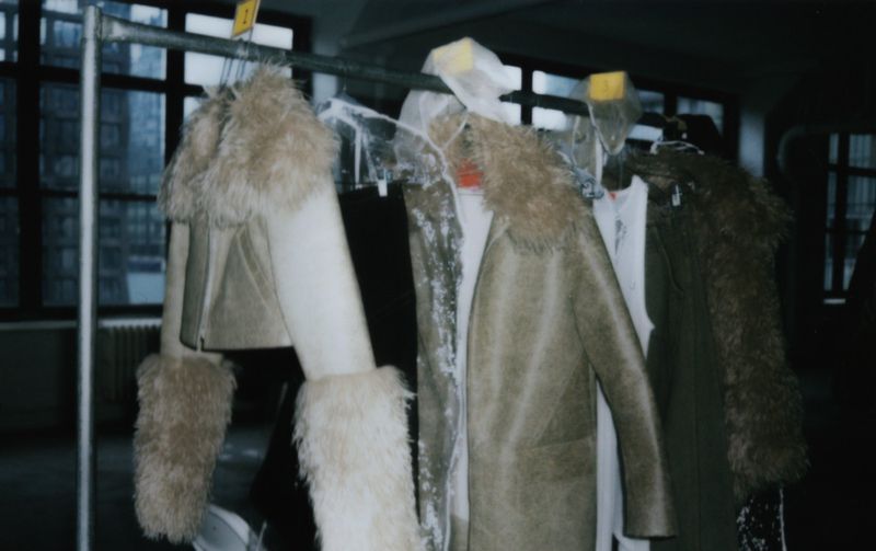 Rack of fur-collared coats in muted earth tones, hung near window light for fashion or retail display, showcasing outerwear.