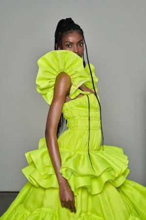 Elegant woman in a vibrant, neon-yellow ruffled gown, captured in a medium shot against a neutral backdrop. Fashion editorial.