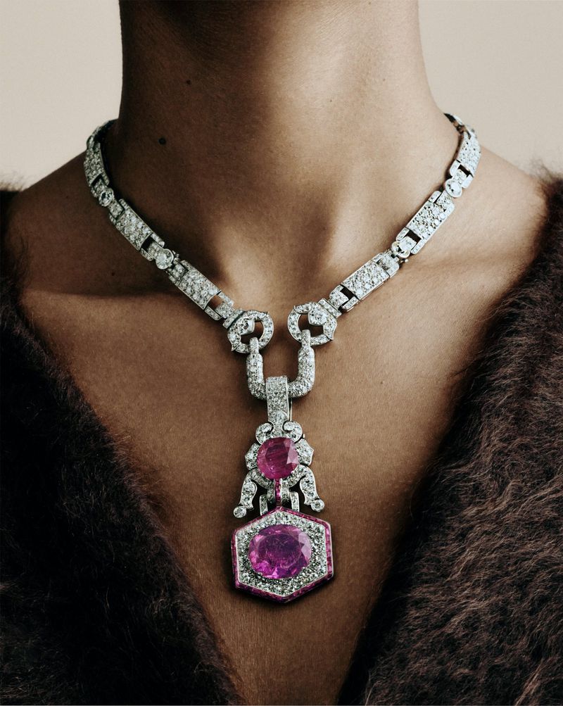 Elegant close-up shot of a dark-skinned person wearing a glittering silver necklace with pink gemstones against a neutral background.
