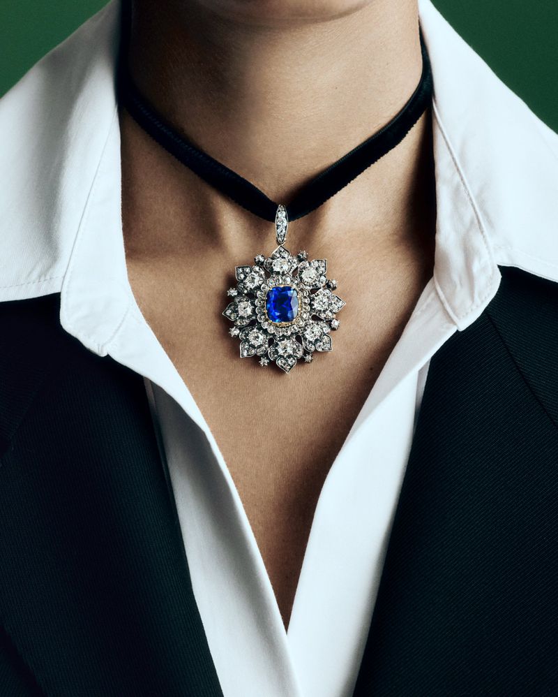 Close-up of a woman wearing a statement choker necklace with a large blue and white jewel pendant, paired with a crisp white shirt and black blazer.