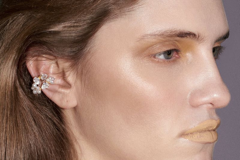 Close-up of a woman's face with an ornate ear cuff featuring pearls and crystals, highlighting beauty and fashion.