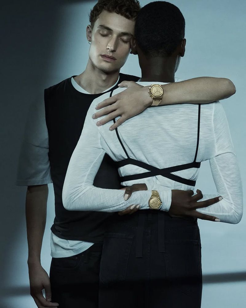 Two people embracing wearing watches. One person faces away from the camera wearing a white top and the other faces forward.
