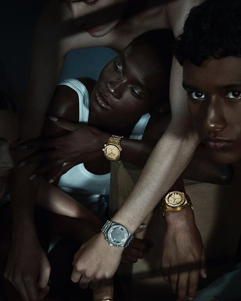Editorial shot features four people, with watches prominently displayed in a dimly lit indoor studio, highlighting fashion and style.