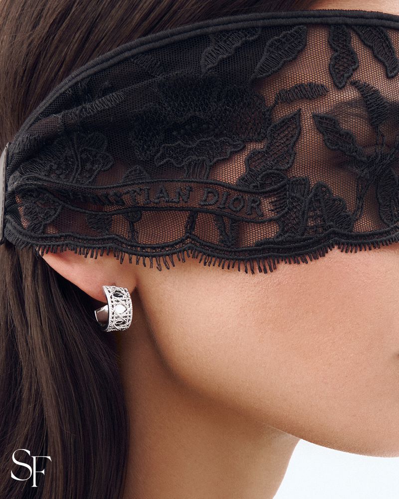 Close-up of woman wearing black lace Christian Dior blindfold and silver hoop earring; beauty, fashion, and skincare concept.