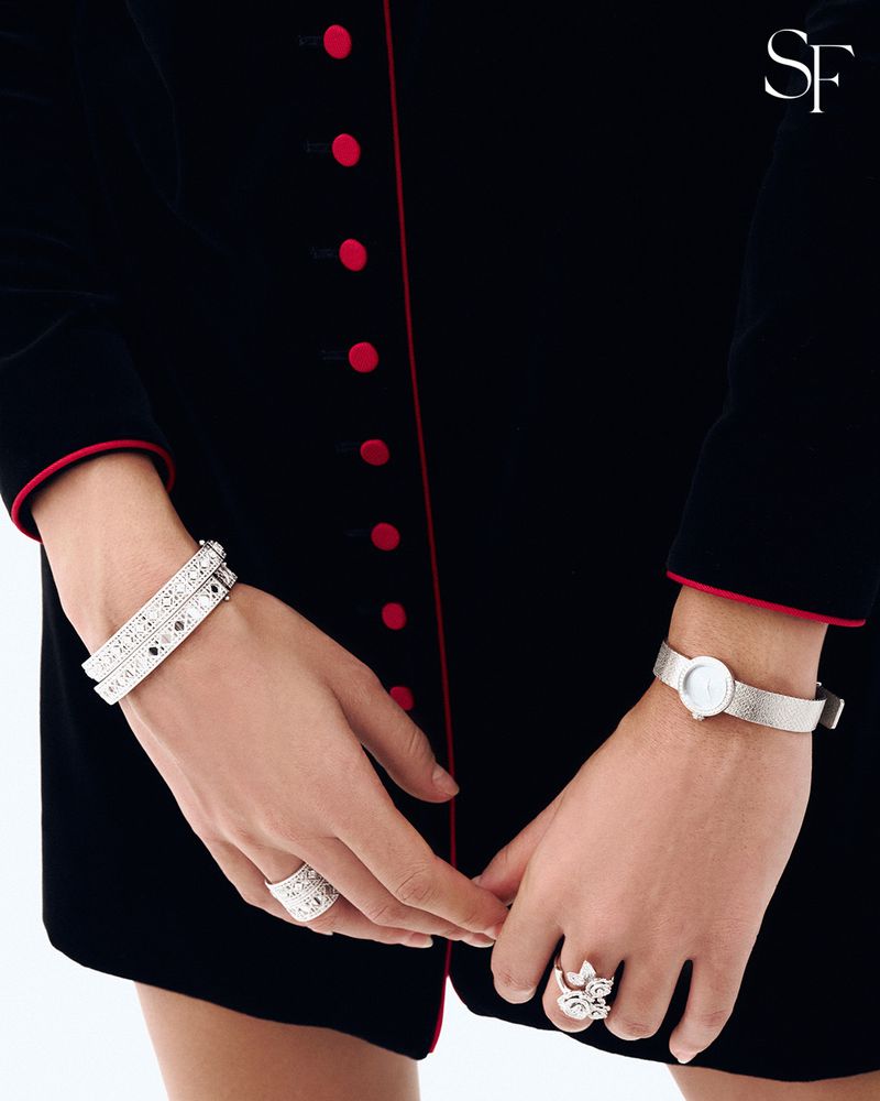 Close-up of a person's hands adorned with bracelets and rings, wearing a black dress with red trim, showcasing fashion jewelry.