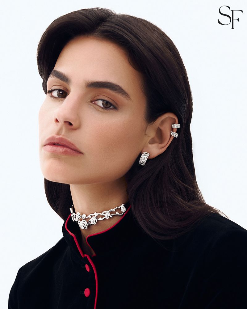 Model wearing a sculpted silver rose choker, diamond ear cuffs, and a black jacket with pink trim against a white background.