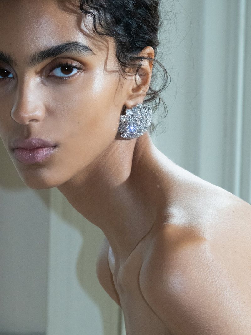 Close-up shot of a fair-skinned woman with curly hair wearing sparkling earrings, set against a neutral background with natural lighting.